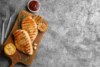 Tasty grilled chicken fillets with garlic, lemon and sauce on grey table, flat lay. Space for text