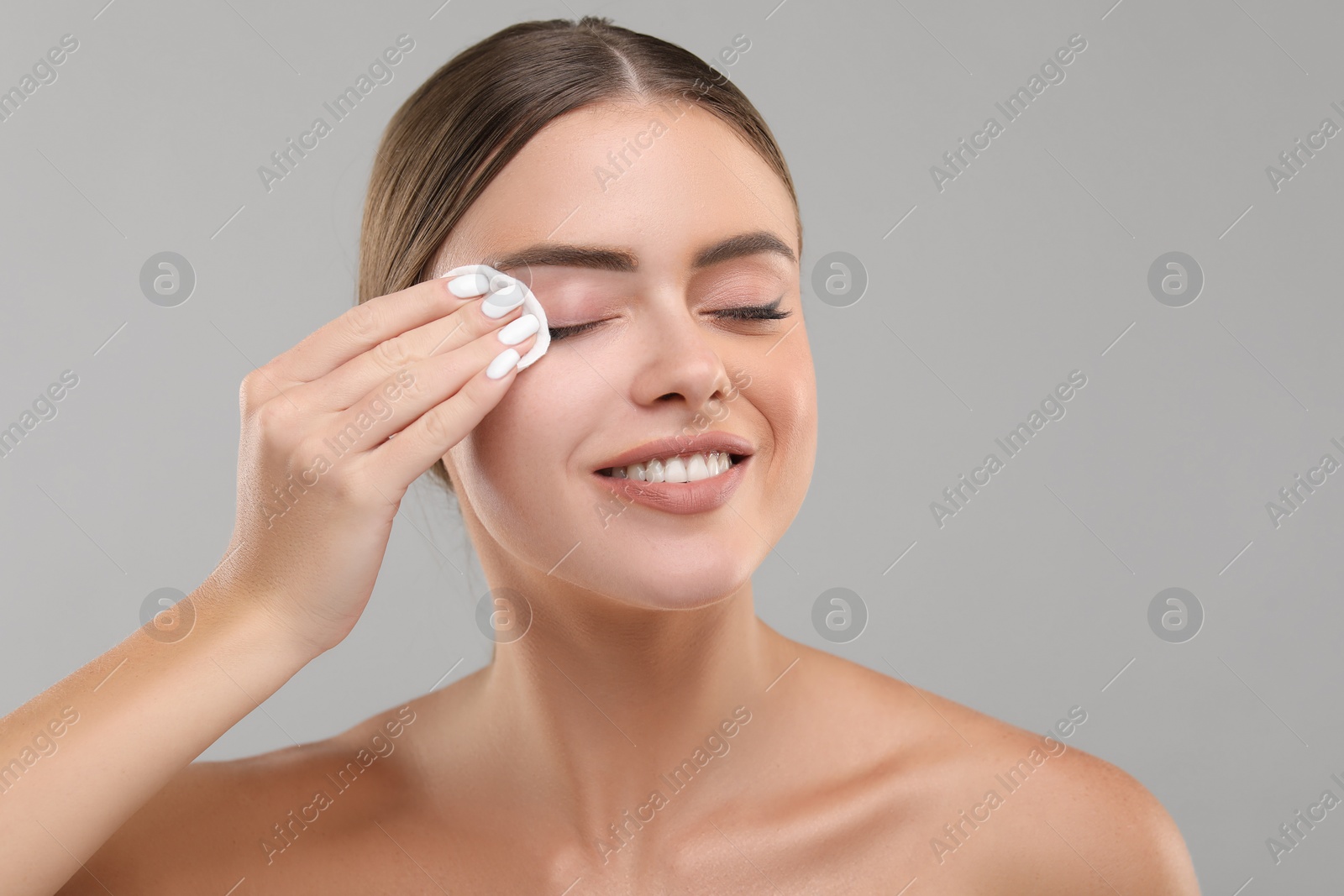 Photo of Beautiful woman removing makeup with cotton pad on grey background