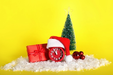 Photo of Alarm clock with Christmas decor on yellow background. New Year countdown
