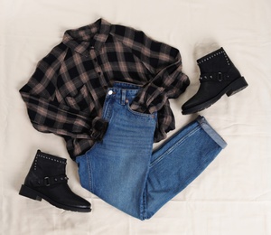 Flat lay composition with jeans, flannel shirt and shoes on white fabric