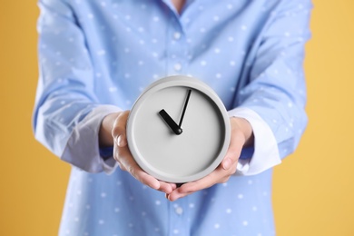 Young woman holding alarm clock on color background. Time concept