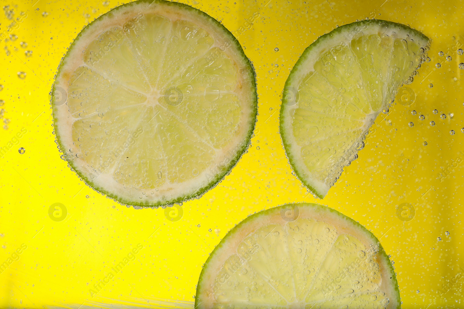 Photo of Juicy lime slices in soda water against yellow background, closeup