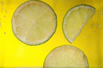 Juicy lime slices in soda water against yellow background, closeup