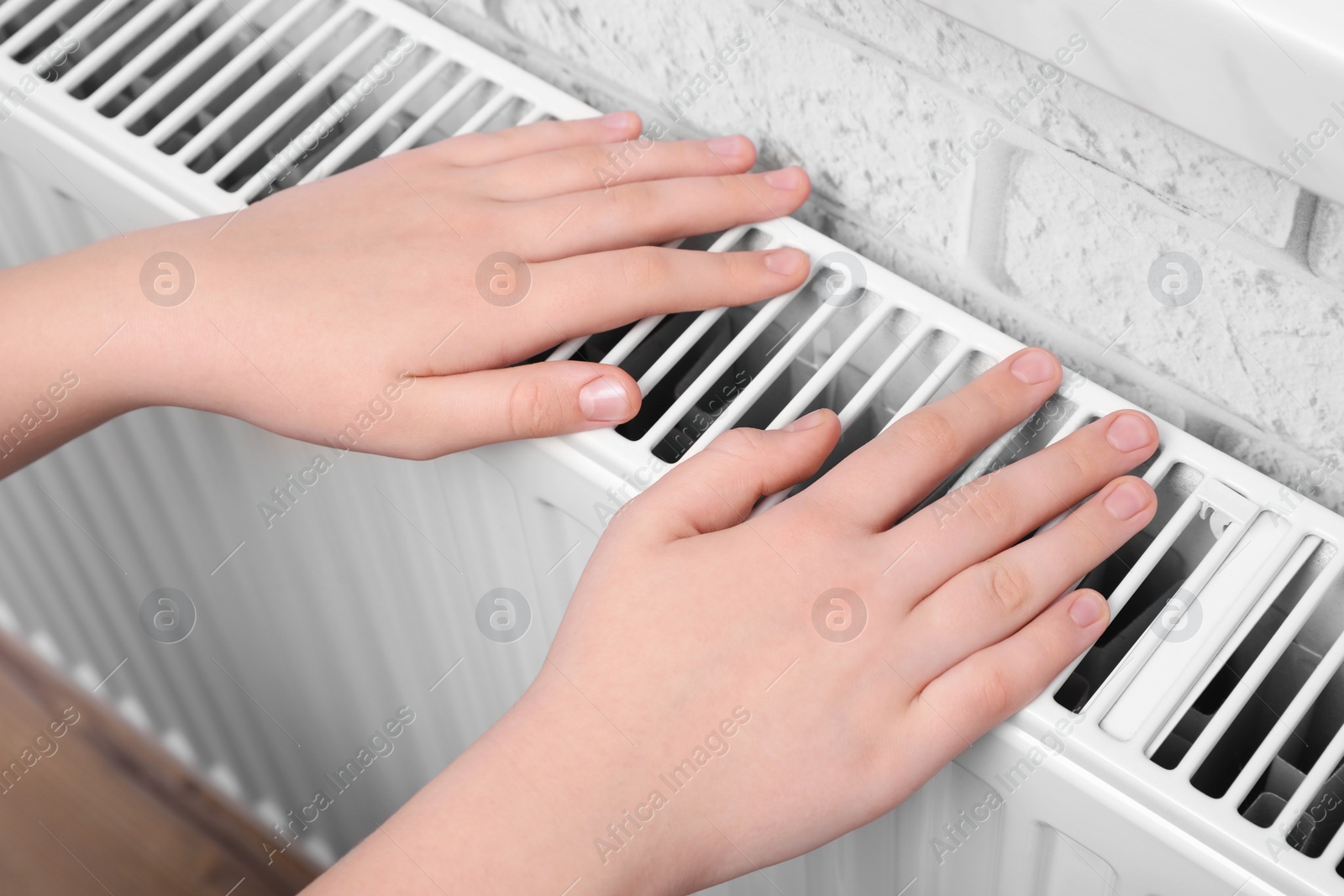 Photo of Girl warming hands on heating radiator indoors, closeup