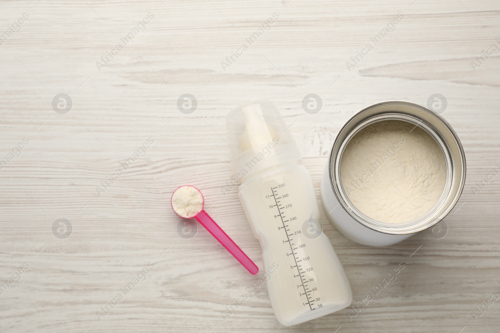 Photo of Feeding bottle with infant formula and powder on white wooden table, flat lay. Space for text