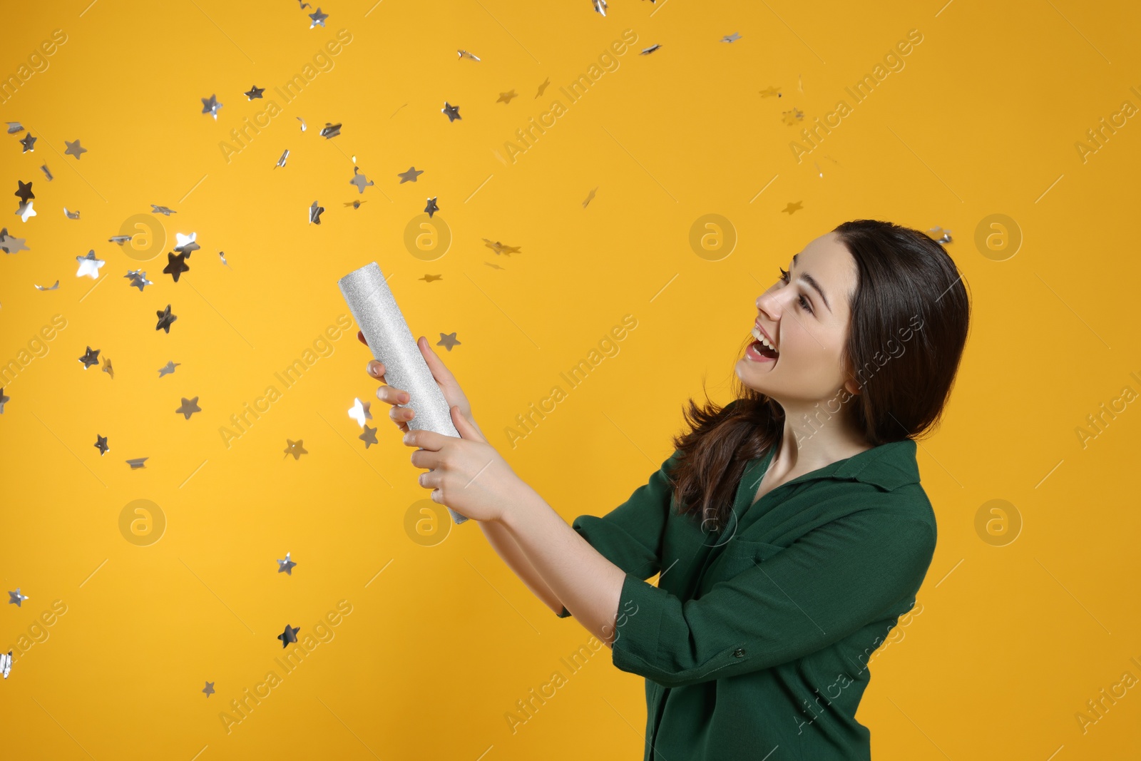 Photo of Young woman blowing up party popper on yellow background