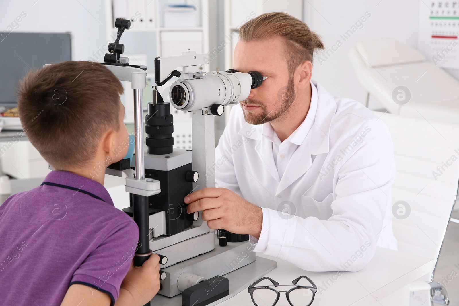 Photo of Children's doctor examining little boy with slit lamp in clinic