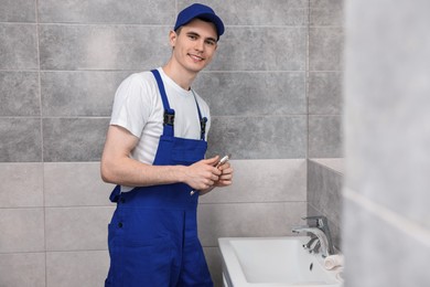 Photo of Smiling plumber repairing metal faucet with spanner in bathroom