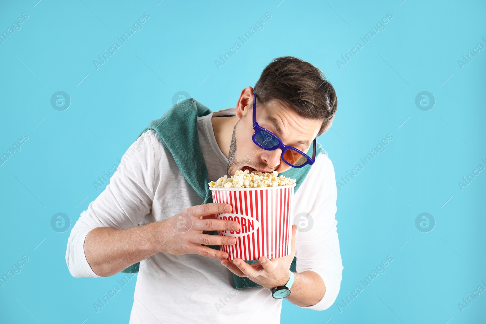 Photo of Man with 3D glasses eating tasty popcorn on color background