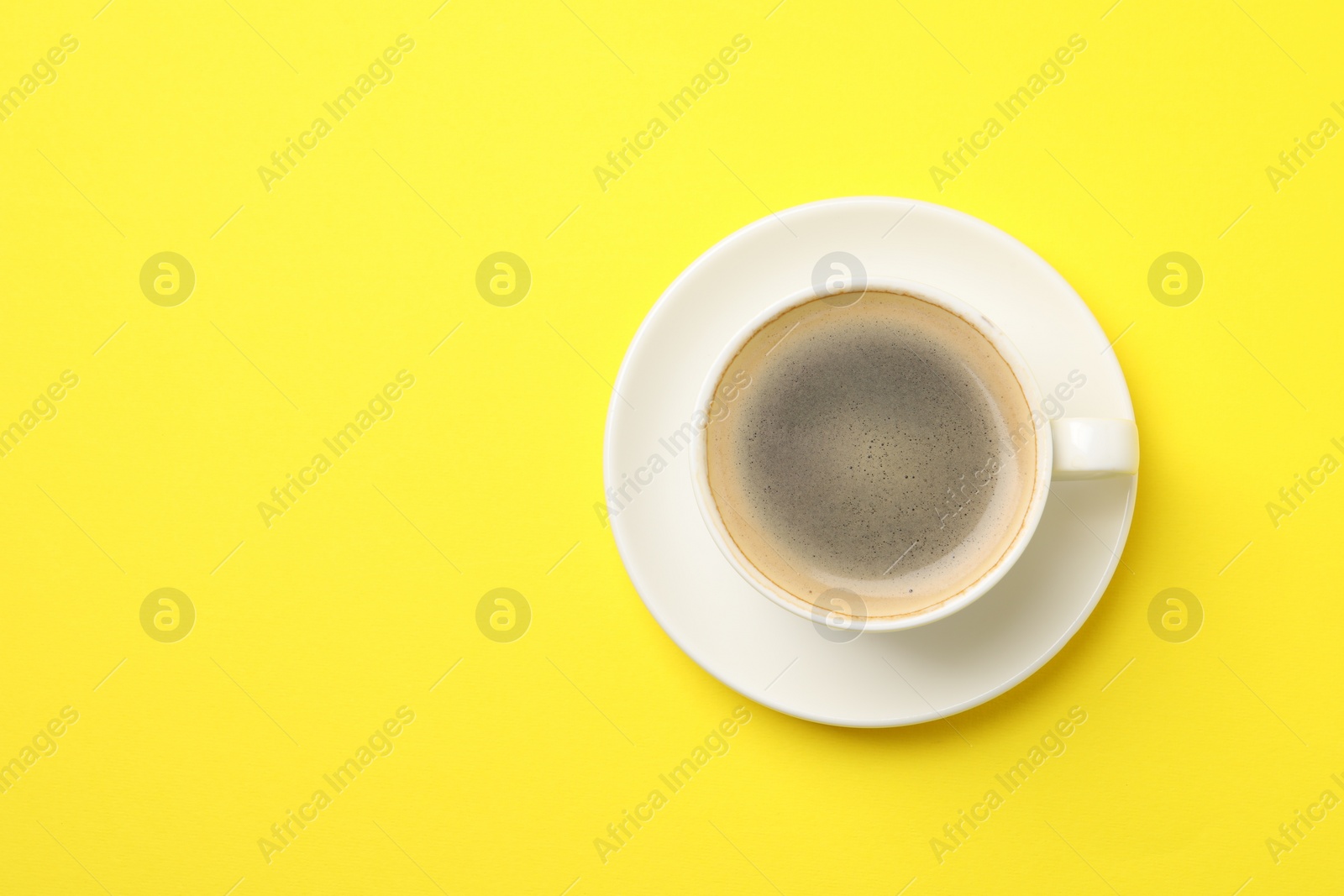 Photo of Aromatic coffee in cup on yellow background, top view. Space for text