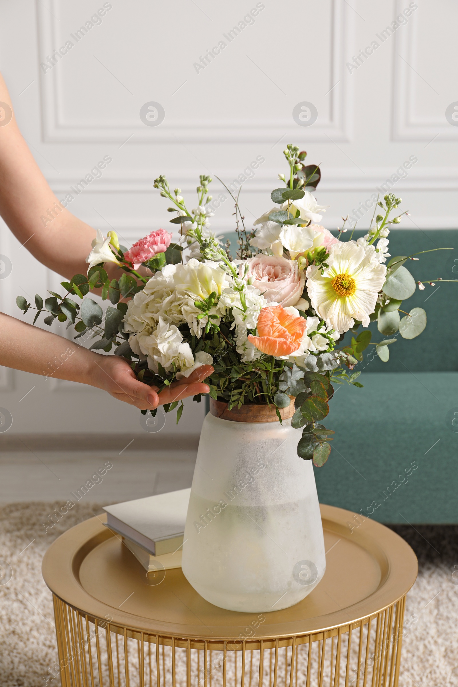 Photo of Woman arranging bouquet of beautiful flowers in vase indoors, closeup