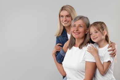 Photo of Three generations. Happy grandmother, her daughter and granddaughter on light gray background, space for text