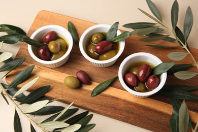 Photo of Bowls with different ripe olives and leaves on beige background
