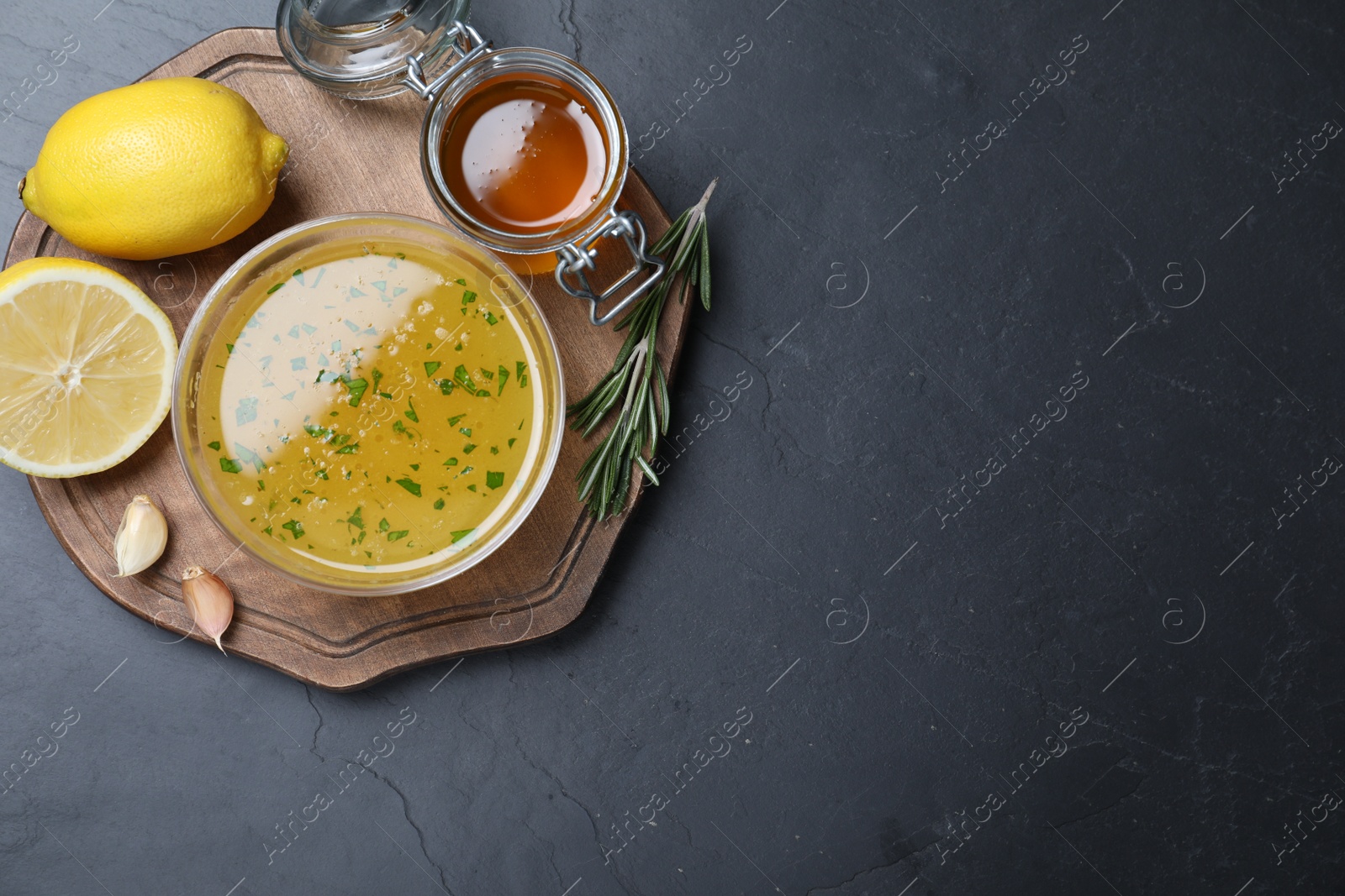 Photo of Bowl of lemon sauce and ingredients on dark table, top view with space for text. Delicious salad dressing