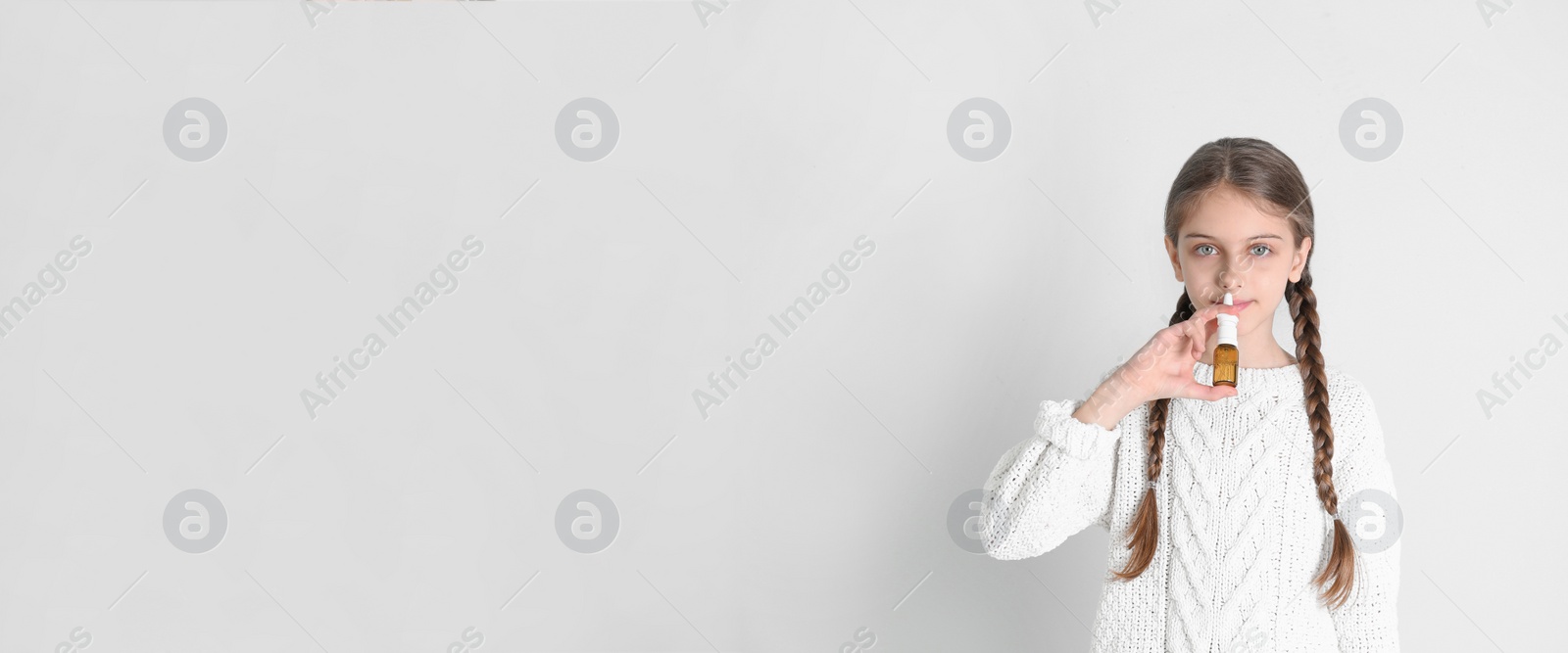 Photo of Sick little girl using nasal spray on white background