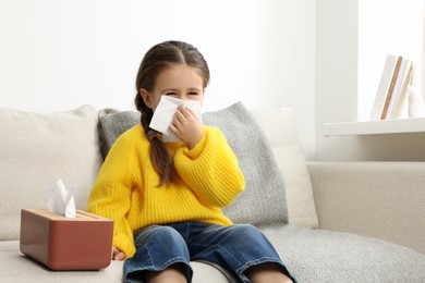 Photo of Girl blowing nose in tissue on sofa in room. Cold symptoms