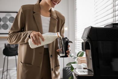 Young woman pouring milk into container near modern coffee machine in office, closeup