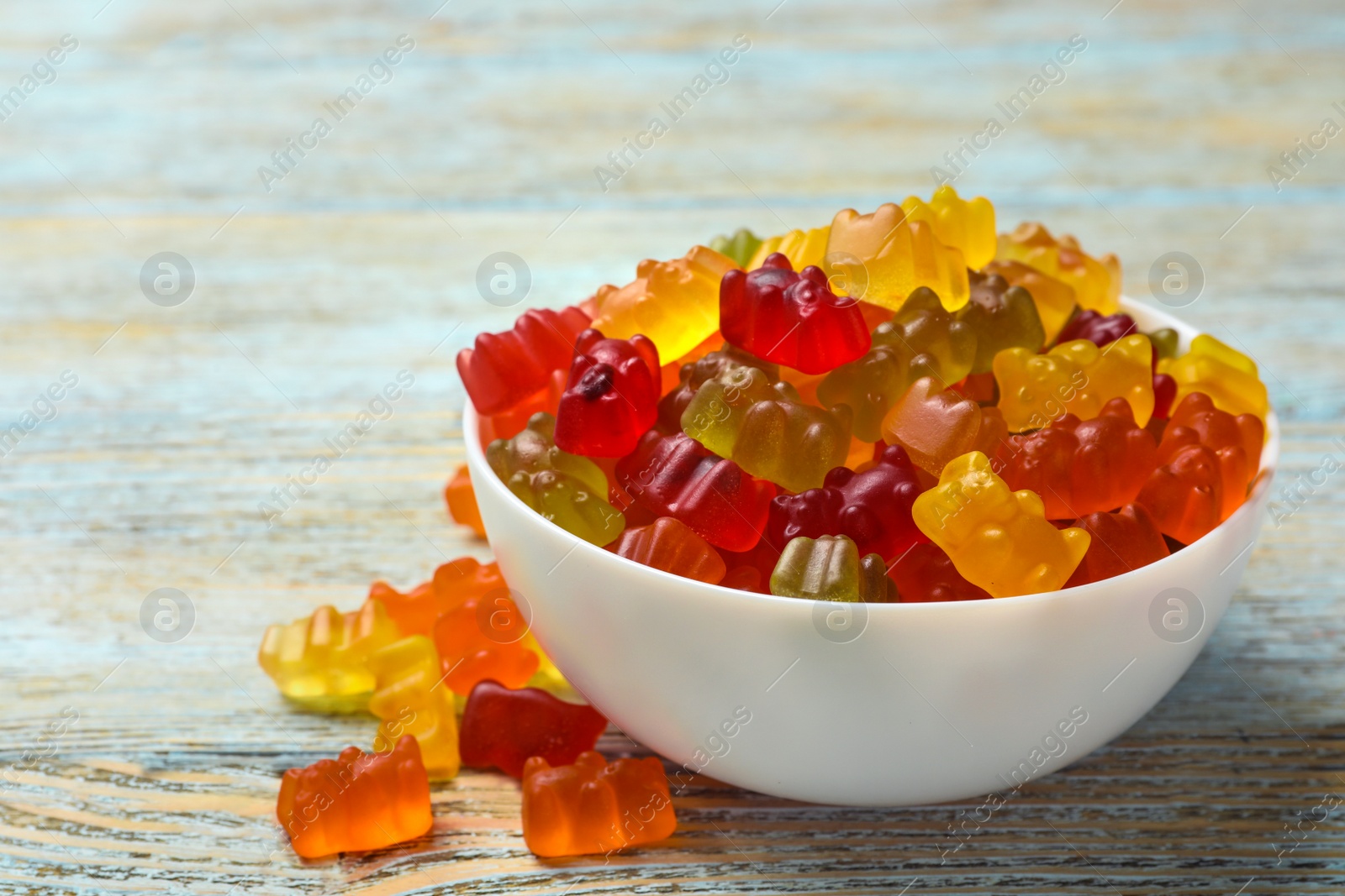 Photo of Bowl with delicious bright jelly bears on wooden table, space for text