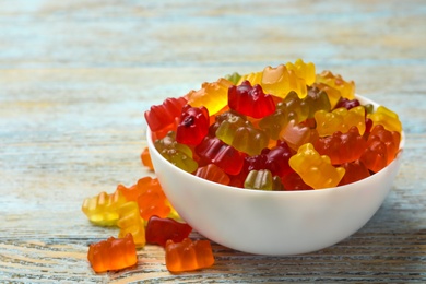 Photo of Bowl with delicious bright jelly bears on wooden table, space for text