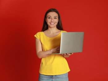 Photo of Young woman with modern laptop on red background