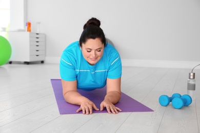 Photo of Overweight woman doing plank exercise on mat in gym