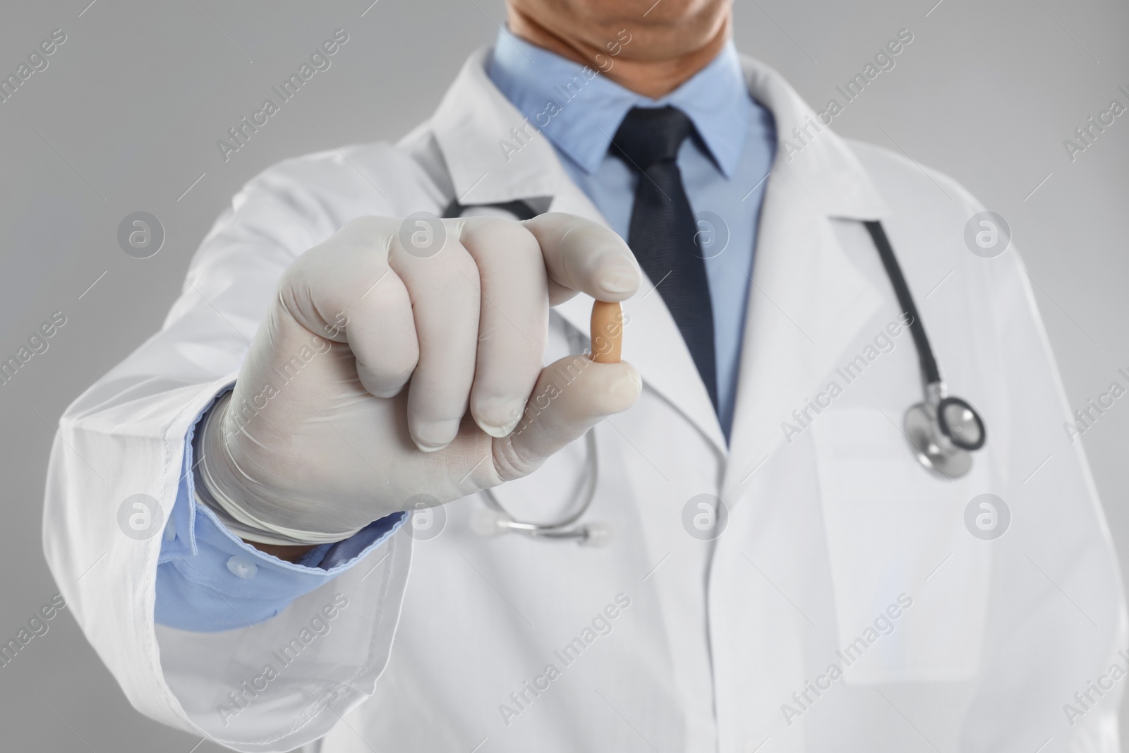 Photo of Doctor holding suppository for hemorrhoid treatment on light grey background, closeup