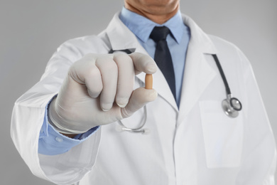 Photo of Doctor holding suppository for hemorrhoid treatment on light grey background, closeup