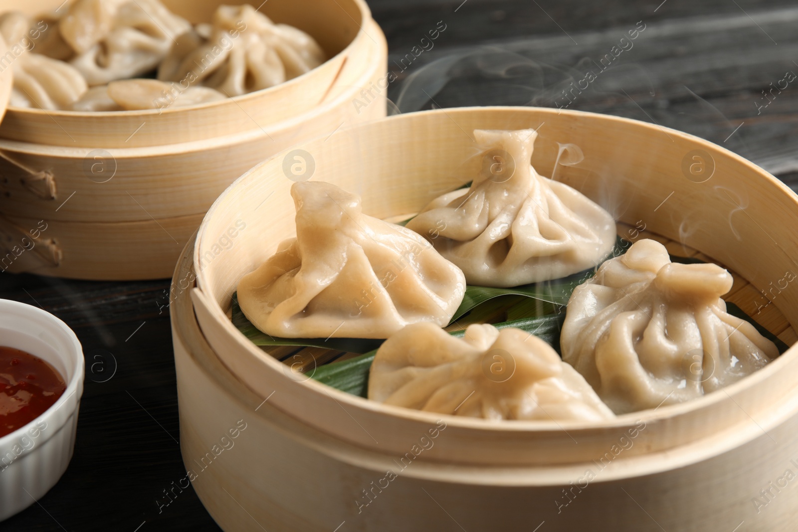 Photo of Bamboo steamers with tasty baozi dumplings and bowl of sauce on table