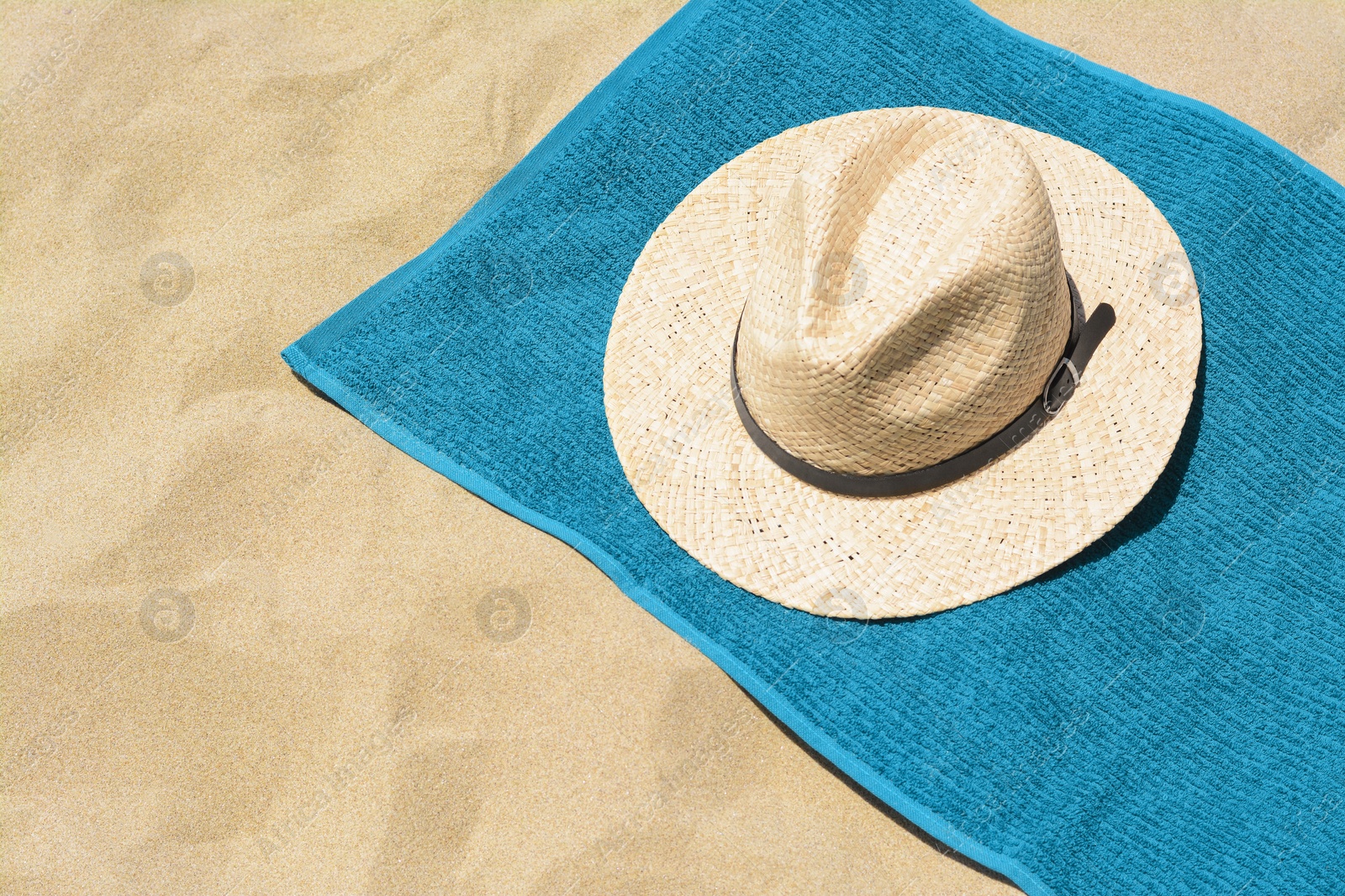 Photo of Soft blue towel and straw hat on sandy beach