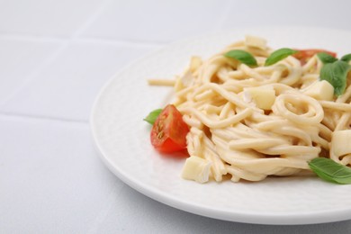 Delicious pasta with brie cheese, tomatoes and basil leaves on white tiled table, closeup. Space for text