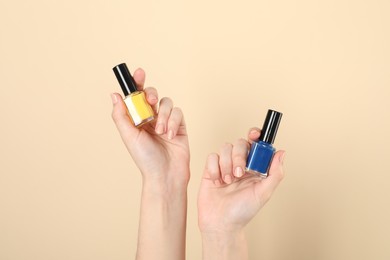 Photo of Woman holding nail polishes on beige background, closeup