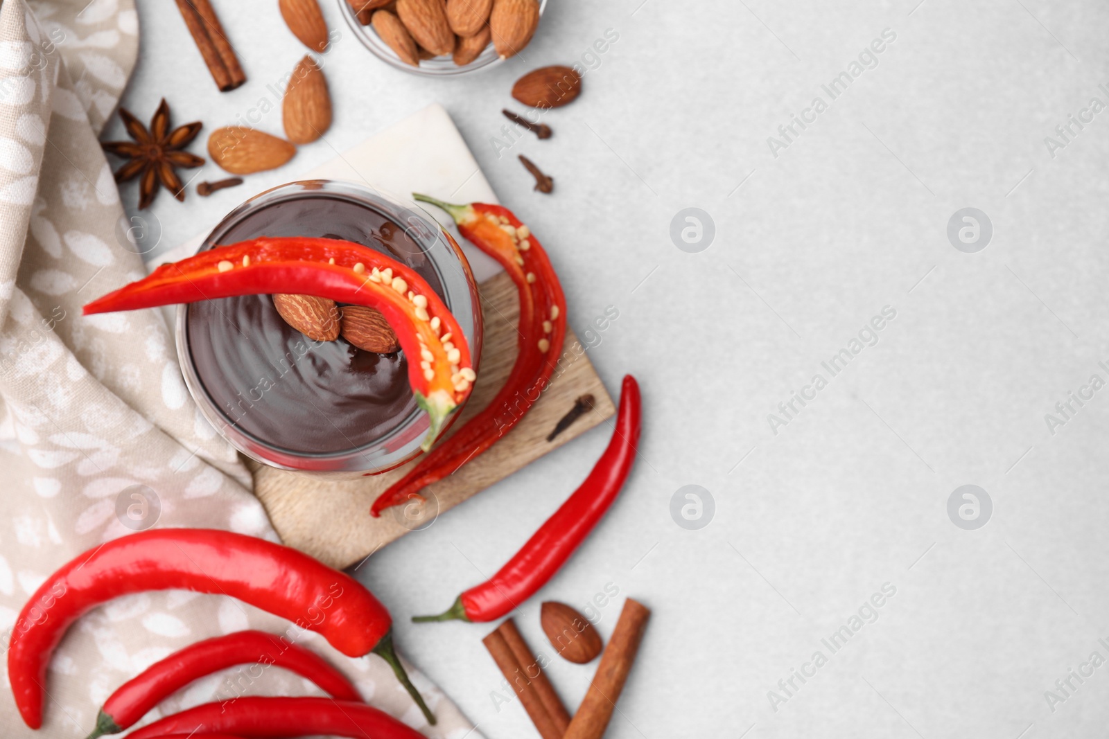 Photo of Glass of hot chocolate with chili pepper and almonds on white table, flat lay. Space for text