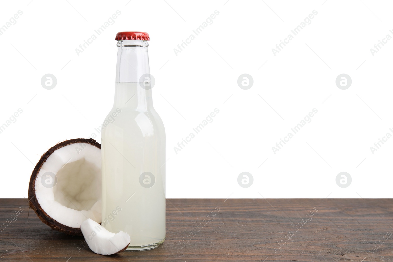 Photo of Delicious kombucha in glass bottle and coconut on wooden table against white background, space for text