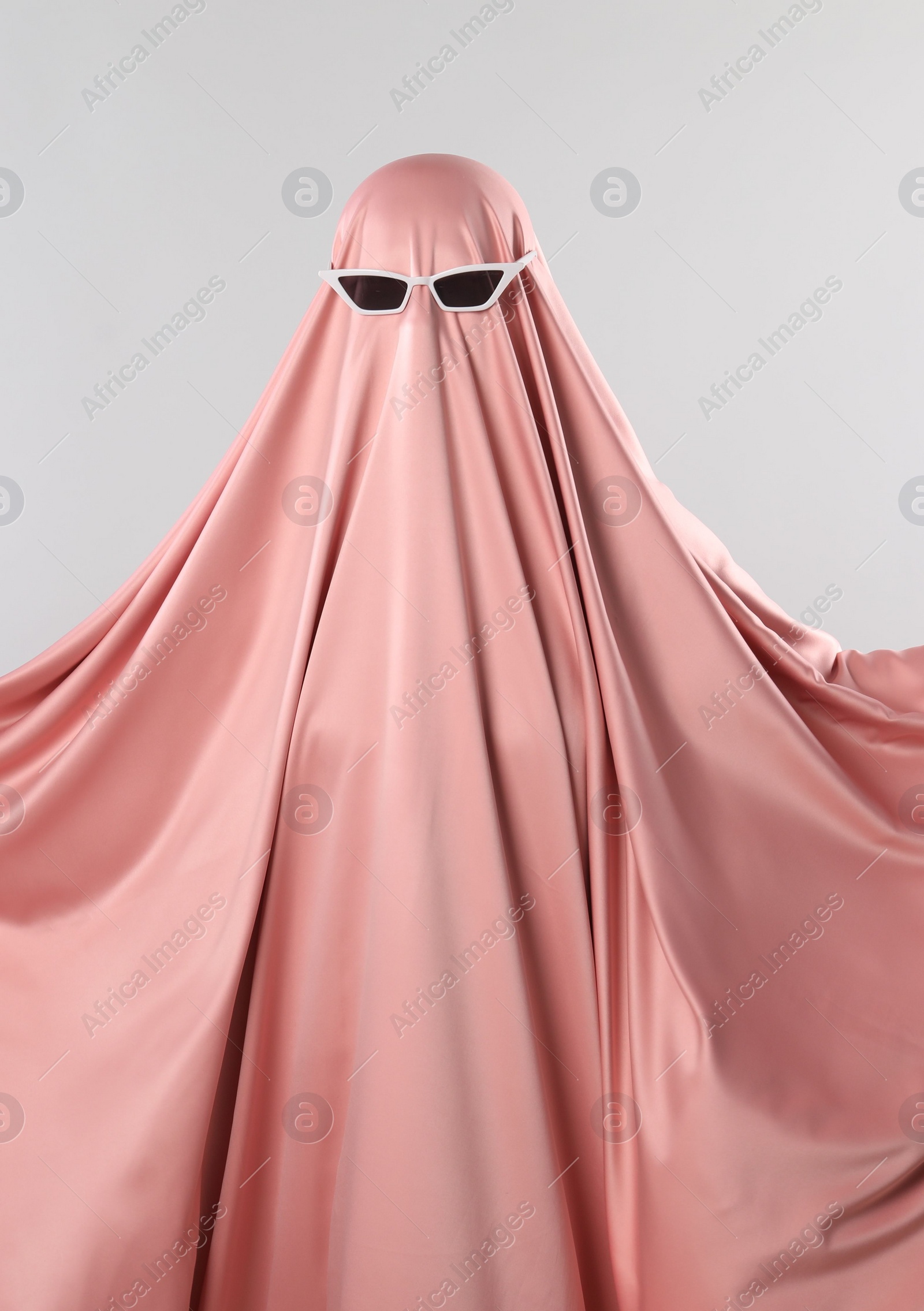 Photo of Glamorous ghost. Woman in pink sheet with sunglasses on light grey background