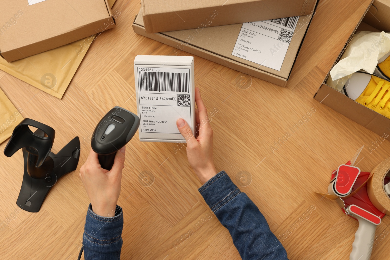 Photo of Woman with scanner reading parcel barcode at wooden table, top view. Online store