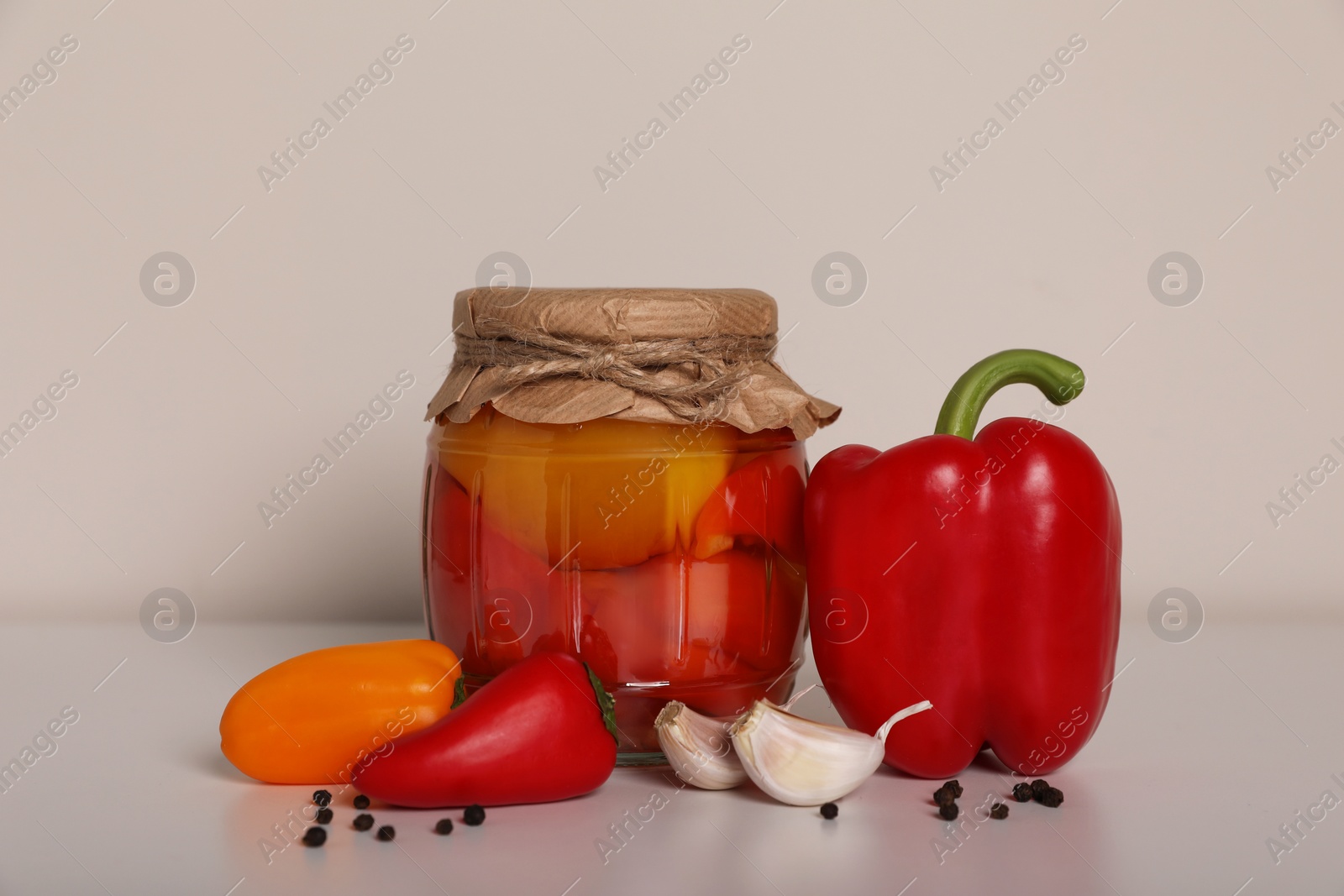 Photo of Tasty pickled peppers, fresh vegetables and garlic on white table