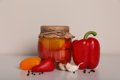 Photo of Tasty pickled peppers, fresh vegetables and garlic on white table