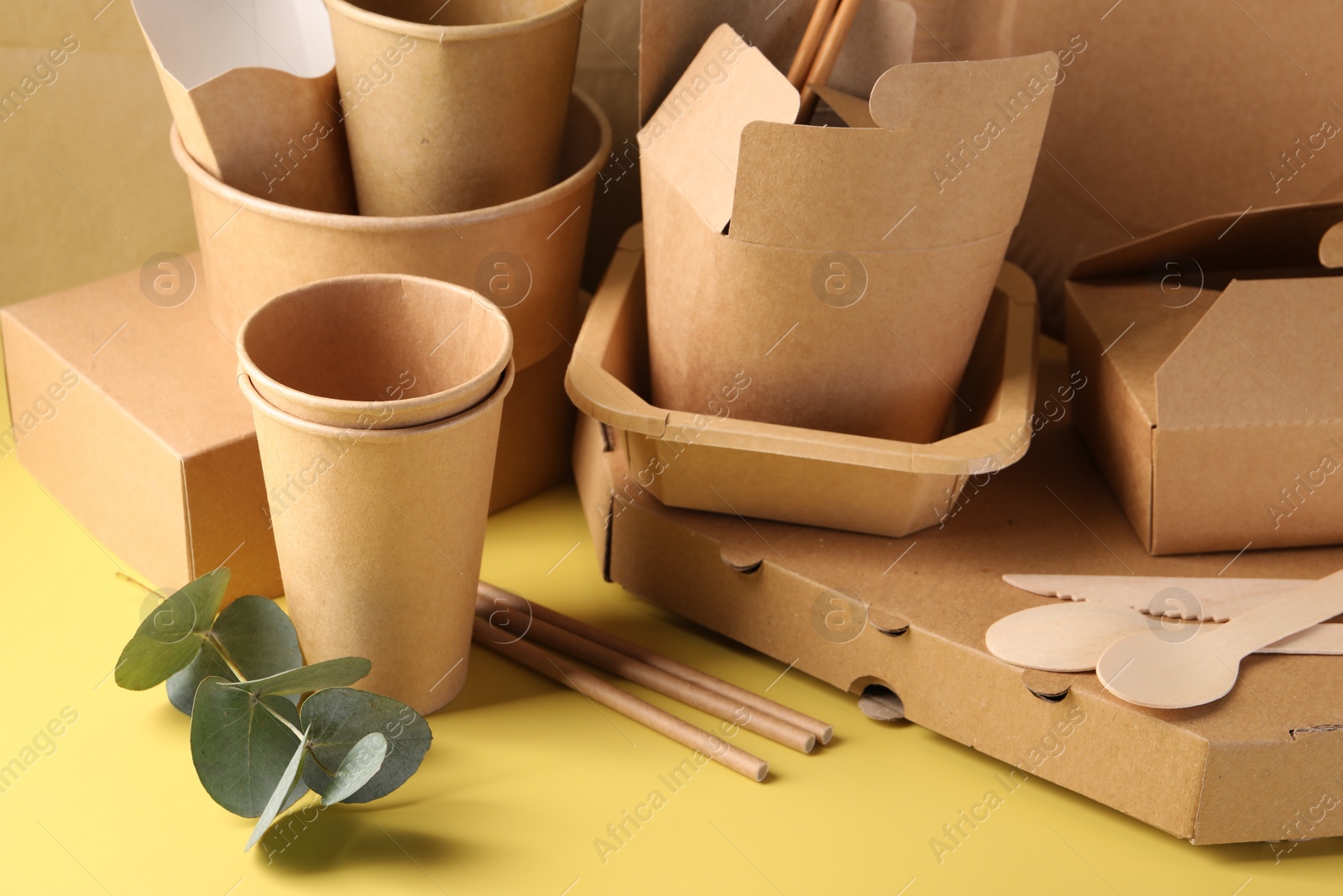 Photo of Eco friendly food packaging. Paper containers, tableware and eucalyptus leaves on pale yellow background