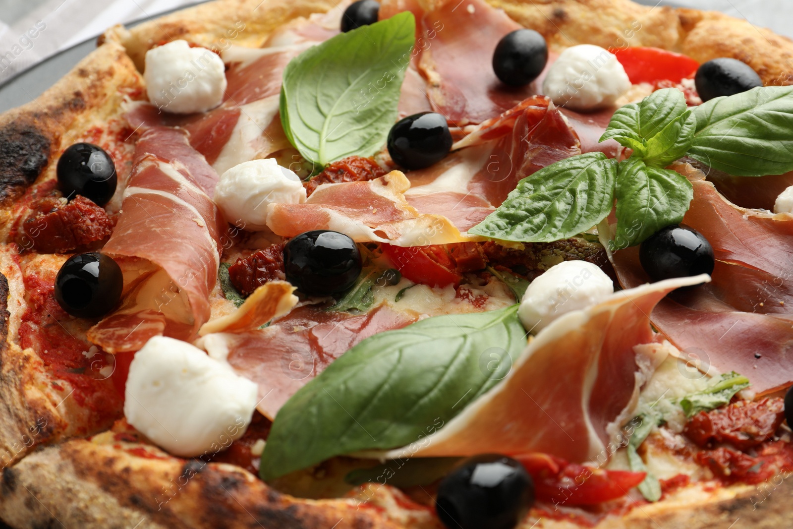 Photo of Tasty pizza with cured ham, olives, mozzarella cheese, sun-dried tomato and basil, closeup