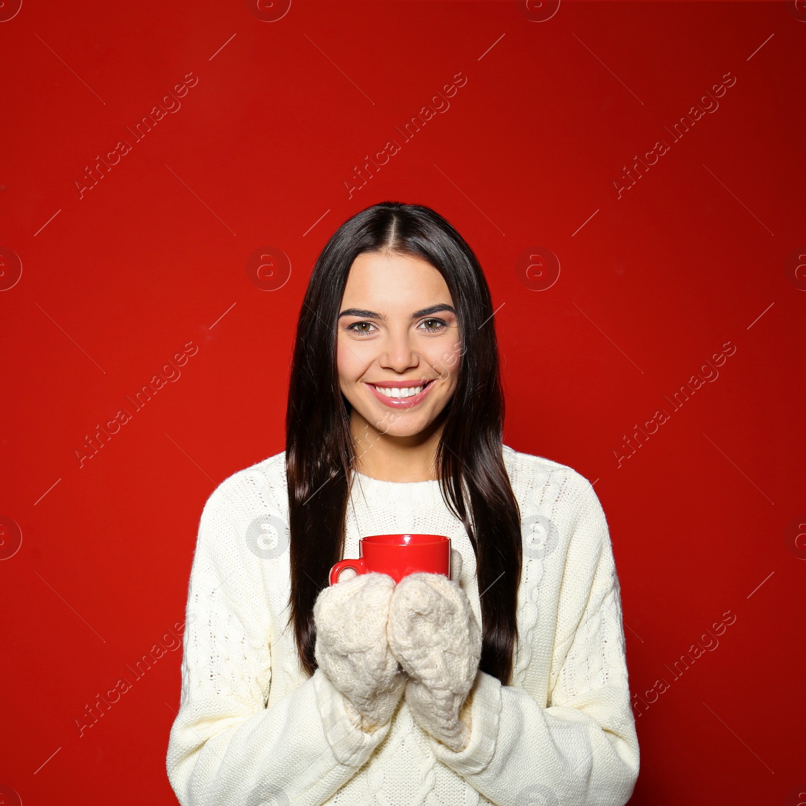 Photo of Young woman in warm sweater with cup of hot drink on red background