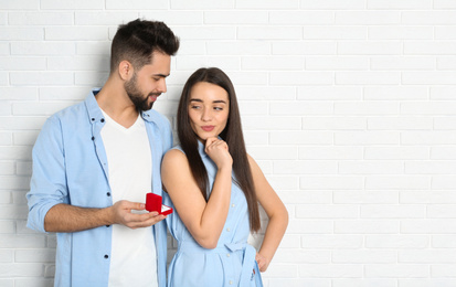Photo of Man with engagement ring making marriage proposal to girlfriend near white brick wall