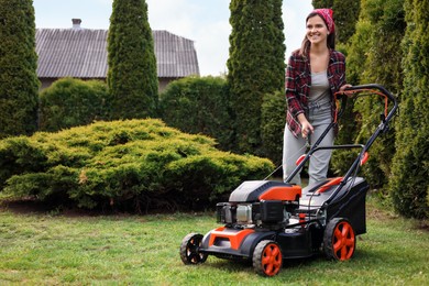 Photo of Smiling woman cutting green grass with lawn mower in garden