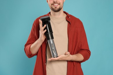 Smiling man holding sous vide cooker on light blue background, closeup