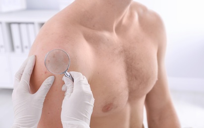 Dermatologist examining patient with magnifying glass in clinic