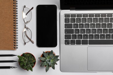 Modern laptop, houseplants, glasses and smartphone on white table, flat lay