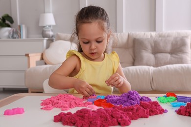 Photo of Cute little girl playing with bright kinetic sand at table in room