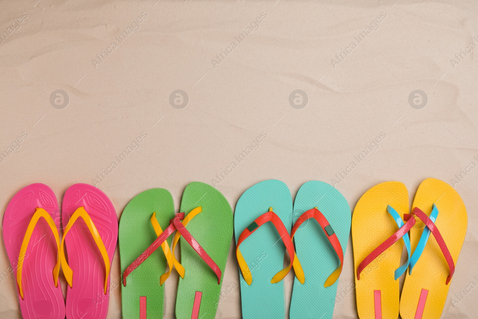 Photo of Different bright flip flops on sand, flat lay. Space for text