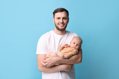 Father with his cute baby on light blue background