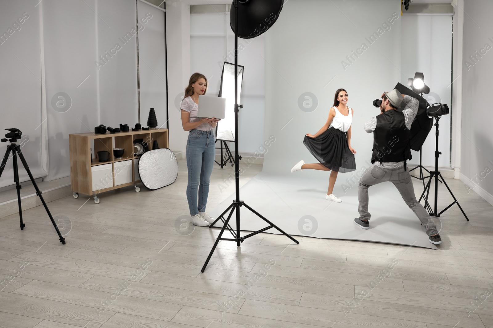 Photo of Professional photographer with assistant taking picture of young woman in modern studio