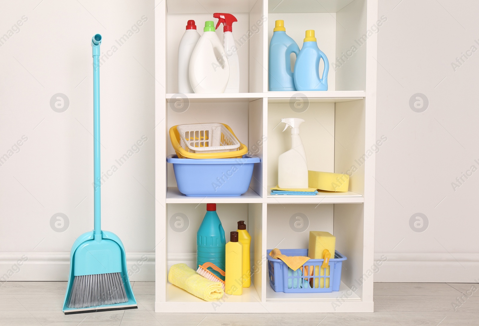 Photo of Shelving unit with detergents and cleaning tools near white wall indoors